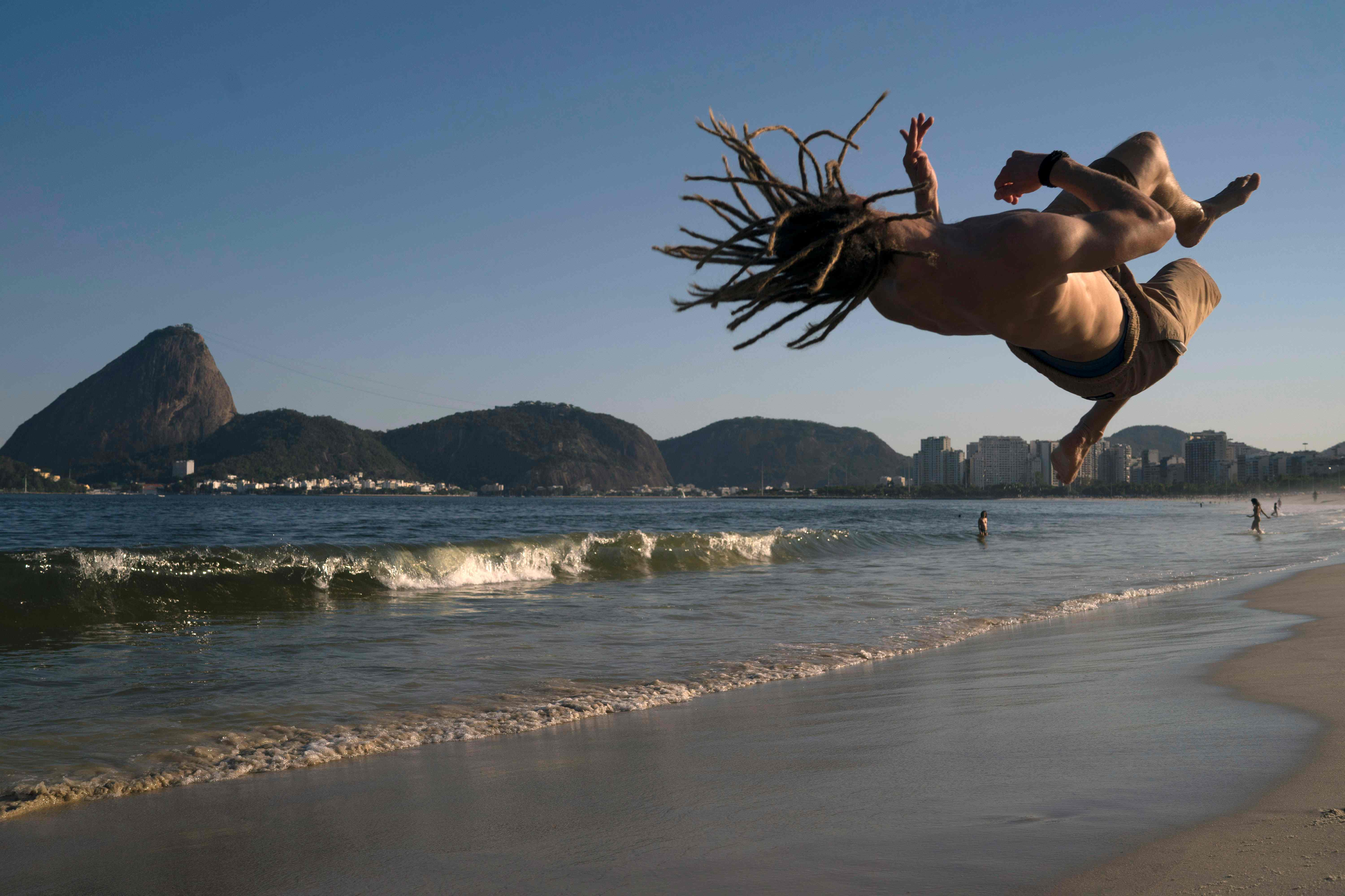 129 German national Alex Leist,  jumps backdropped by the Sugar Loaf mount during his mixed training of Brazilian capoeira fight and acrobatics at Flamengo beach in Rio de Janeiro, Brazil, on November 16, 2017.  / AFP PHOTO / LEO CORREA